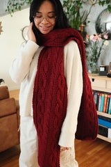 Woman in cream outfit wears cranberry red crochet scarf with cables.  thumbnail