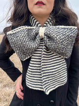 Close-up of knit scarf in the shape of a bow, with striped ends and a checkered middle.  thumbnail