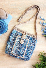 Blue and tan crochet bag laying on pale wooden backdrop. Bag has long handle and front pocket.  thumbnail