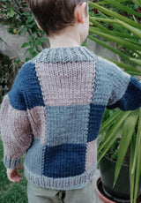 Back view of child's patchwork knit cardigan, with blocks of dark blue, medium blue, and tan.  thumbnail