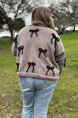 Back view of tan knitted cardigan with applied bows in black.  thumbnail