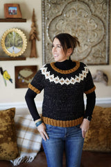 Woman with charcoal knit sweater with white patterned yoke and mustard ribbing stands in living room.  thumbnail