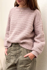 Zoomed in photo of young woman wearing pale pink crochet sweater and khaki pants.  thumbnail