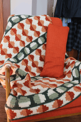 Crochet throw with circle motifs in shades of rust, green, and cream draped over orange chair with matching pillow.  thumbnail