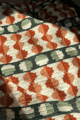 Close up of afghan, showing circle motifs. Circles are split in half with either two shades of orange, or sage and cream. There are stripes of dark green behind the sage  cream circles.  thumbnail