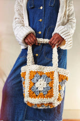 Woman in cream cardigan and denim dress holds smaller granny square bag in cream, mustard, and grey.  thumbnail