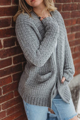 Close up of woman wearing crochet cardigan leaning against a red brick wall.  thumbnail