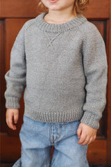 Close up of a toddler wearing a pale grey raglan sweater, with blue jeans.  thumbnail