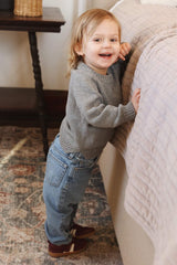 Side view of toddler wearing grey pullover sweater, showing split hem. The child wears it with blue jeans and brown sneakers.  thumbnail