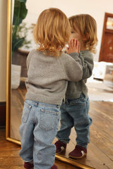 Back view of toddler wearing grey pullover sweater, facing mirror so front view of sweater is partially visible.  thumbnail