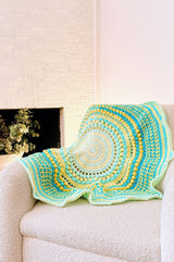 Circular crochet afghan in yellow and aqua green, draped over a cream armchair.  thumbnail