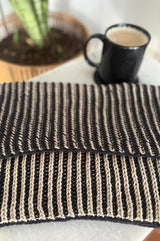 Flat lay of two color cowl on end table, with a cup of coffee and a potted plant in the background. The cowl is folded in half and is knit in pale tan and black.  thumbnail