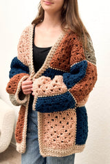 Young woman wears oversize crochet cardigan with large solid colored granny squares in pale pink, rusty orange, an, and dark blue.  thumbnail