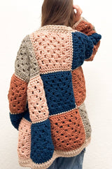 Back view of patchwork granny square cardigan. Squares are arranged in diagonal stripes in taupe, rusty orange, medium blue, and pale pink. The cardigan is trimmed in pale tan.  thumbnail