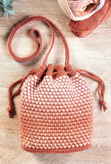 Crochet bucket bag in shades of rusty orange is laid on a light wood table top.  thumbnail