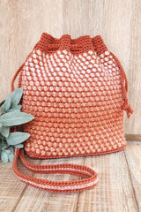 Front view of crochet bag with a textured pattern in pale orange against a rusty orange background color. The bag stands against a wooden backdrop.  thumbnail