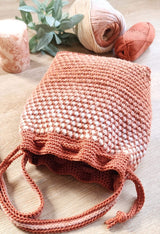 Front view of crochet bucket bag laying down, looking into drawstring top. The long shoulder strap is curled to the side.  thumbnail