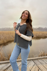 Woman stands on wooden dock in wetland area. She's turned to the side so you can see the split hem on the capelet.  thumbnail
