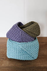 Three crochet baskets sitting inside each other at angles. They are on a dark wooden countertop with a white background.  thumbnail