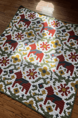 Full view of afghan with white background, brick red horses with dark blue saddles, olive green vines, and mustard yellow, brick red, and dark blue flowers.  thumbnail