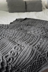 Grey cabled afghan laid on bed with white bedding.  thumbnail