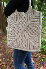 Woman standing sideways wears a rectangular tote bag with all over cables.  thumbnail