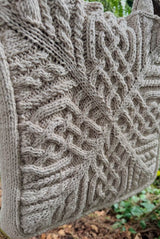 Close up of cabled tote bag, knit in a beige yarn. The cables radiate out from the center of the bag.  thumbnail