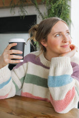 Close up of striped sweater, showing ribbed cuffs and neckline, as well as different textures in yarn. Background cream is smooth, contrast stripes are a fuzzy yarn.  thumbnail