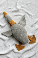Crochet goose in soft grey with warm yellow beak, feet, and kerchief. The goose body is softly stuffed and lays on a white blanket.  thumbnail
