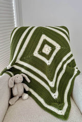 Crochet baby blanket fraped over beige armchair, with a stuffed bunny propped against the arm. The blanket is worked from the center out in cream and olive green.  thumbnail