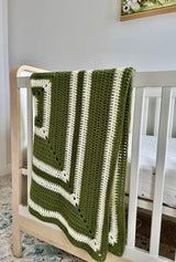Crochet blanket in cream and olive draped over the side of crib.  thumbnail
