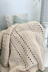 Cream crochet blanket draped over armchair in a neutral living room.  thumbnail