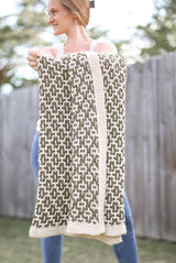 Woman holds crochet throw toward camera. The blanket uses a mosaic crochet colorwork pattern in cream and olive green.  thumbnail