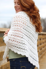 Close up of the side view of a crochet shawl. The shawl is white with bands of bobbles and open shell pattern.  thumbnail