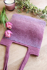 Crochet tote bag with shoulder-length straps is laid with straps facing viewer. An unlit candle and flowers frame the bottom of the bag.  thumbnail