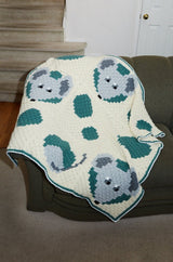 Crochet blanket laid over couch indoors. The blanket is worked in C2C crochet and has cartoon mice peeking from "holes" on a swiss cheese background.  thumbnail