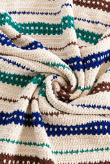Close up of crochet blanket. It's made in cream with stripes of varying widths in green, royal blue, and chocolate brown.  thumbnail
