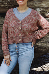 Copped front view of a knit cardigan on a model earing a grey shirt and blue jeans in front of a fallen tree. The cardigan has long sleeves and a cropped body, with wide ribbing at the hem and four large buttons. It's knit in a marled fabric, with one strand of beige and one strand of brownish red.  thumbnail