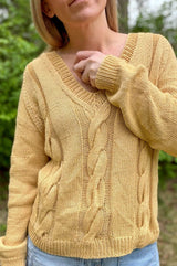 Close up of yellow knit sweater, showing three wide rope cables running down front, between columns of stockinette. The model has her arm crossed over the front to show the plain sleeves and ribbed cuff. thumbnail