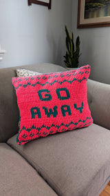 Pink and green crochet pillow sits on a grey couch.  thumbnail