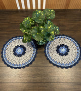 Two matching doilies laid on a dark wood table, with a potted plant in the middle.  thumbnail
