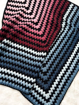 Mitered square crochet blanket laid on a white background. The blanket has stripes of black with a pink to burgundy gradient, and a pale blue to steel blue gradient.  thumbnail