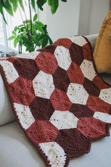 Hexagon motif blanket laid over a white couch, with a yellow throw pillow and a plant in the background.  thumbnail