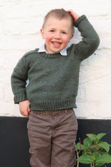 Young boy wears a green sweater over a collared shirt and brown pants.  thumbnail