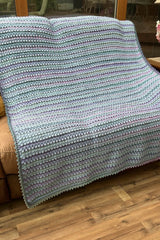 Crochet blanket in sky blue, greens, and purples draped over tan loveseat.  thumbnail
