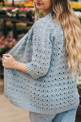 Back and side view of lacy crochet cardigan. It has ribbed trim on the sleeves, hem, and front opening. The woman wearing it is holding the front open.  thumbnail