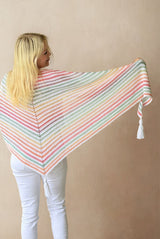 Back view of model holding shawl with the top edge outstretched. The right edge of the shawl is curled and you can see the tassels on that tip and the center point.  thumbnail