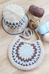Flat lay of crochet bucket hat and bag on pale wooden table. There is a decorative rope knot ball and skeins of yarn on the right of frame.  thumbnail