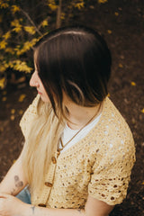 Looking down at shoulder of crochet cardigan, showing v-neck shaping and short sleeves. It's closed with three buttons.  thumbnail
