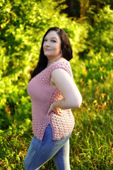 Side view of woman in a pale pink crochet top and blue jeans, standing in lush greenery. The top has cap sleeves and a split hem.  thumbnail